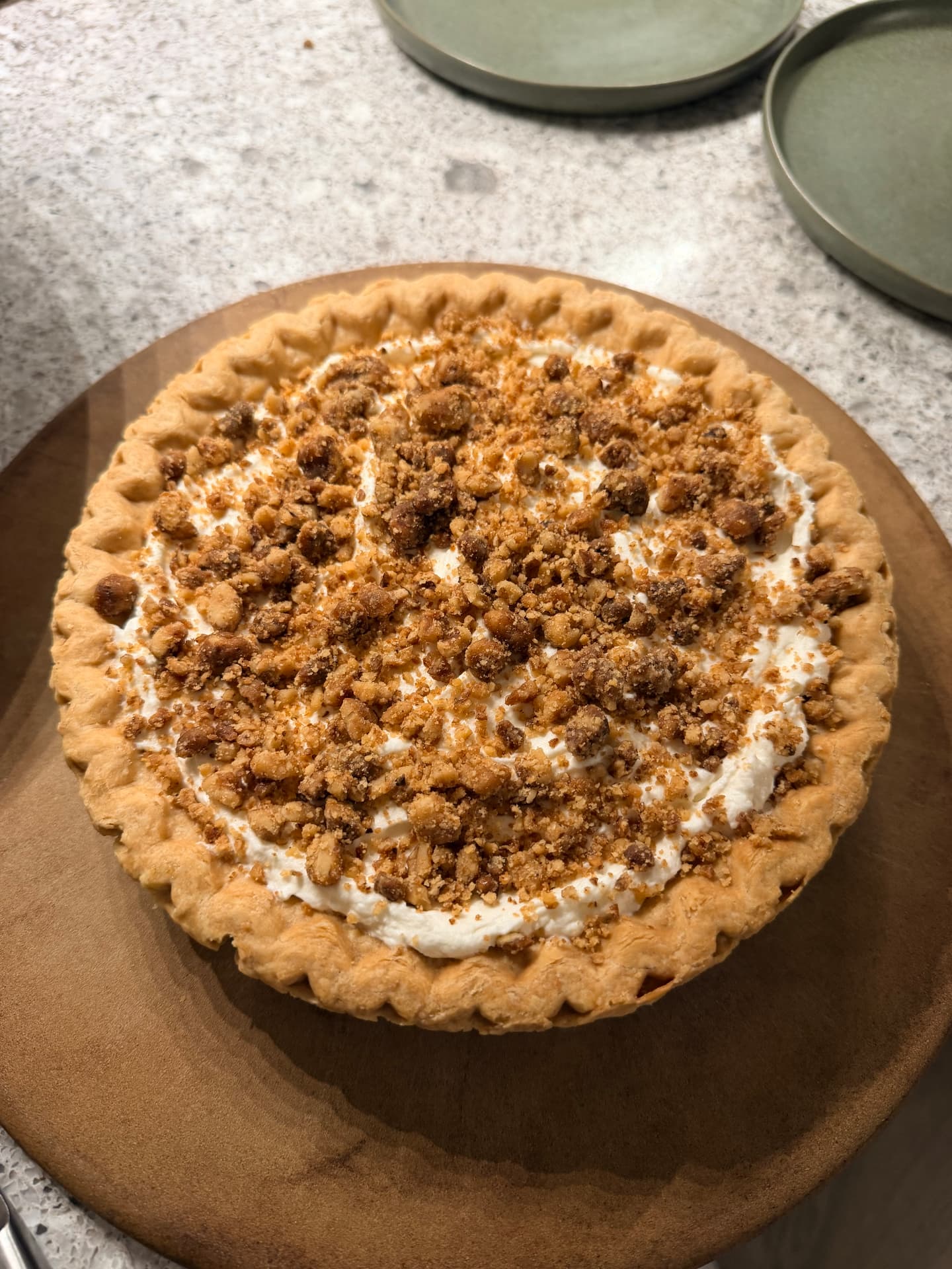 Whole cream pie in a crimped crust topped with whipped cream and candied nut crumble