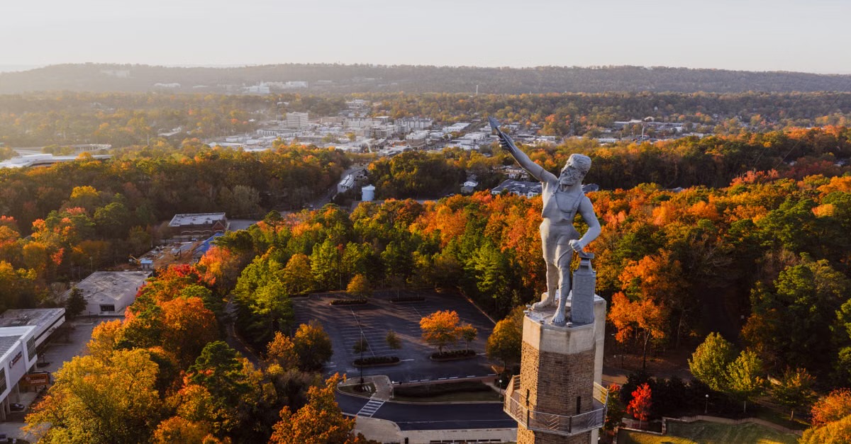 Aerial view of a hilltop statue above autumn treetops and the city below